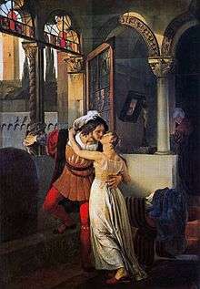 A man and woman kissing, dressed in 16th-century clothes, in a large room with rounded arches and large windows.