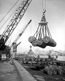Several barrels being lifted off a ship by a crane