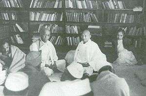 Gandhi seated on a library floor with several other people