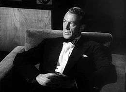 Black and white screen capture of Gary Cooper, seated and wearing a black tuxedo