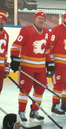 A hockey player in full uniform wearing a toque. He is in a red uniform in white trim with a stylized "C" logo.