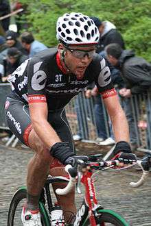 A cyclist riding in the Cervélo jersey. Spectators are visible in the background, looking behind the cyclist.