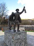A memorial statue showing two men, a miner in difficulty, and a rescuer helping for half carry him. The statue if on a stone plinth.