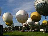 Many white and yellow gas balloons taking off from a grassy field.