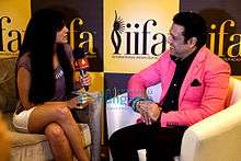 A smiling Govinda, in a pink jacket, being interviewed by a woman