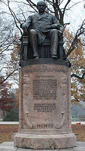 A statue of a middle-aged gentleman sitting in an impressive chair atop a column about five feet tall. "To Marcus Alonzo Hanna" it is marked, with a short message detailing his "efforts for peace between capital and labor" given beneath. A year is finally given in Roman numerals near the base: "MCMVII", or 1907.