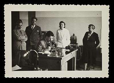 Hans Grüneberg at a microscope surrounded by colleagues in 1952.