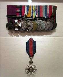 A group of eleven court mounted military medals are displayed in the top half, while a solitary twelfth (the CMG – worn around the neck) hangs below.