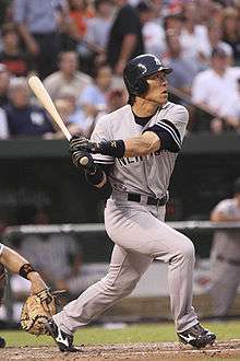 An Asian male wearing a gray uniform with the lettering "NEW YORK" across it, in his after-swing pose.