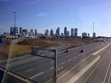 A skyline of tall buildings viewed from an overpass of a freeway