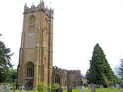 Stone building with arched windows and square tower. In the foreground are gravestones.