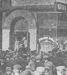 Storefront and arched doorway with a large crowd in the street