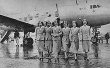 A black-and-white photograph of a Martin 2-0-2 aircraft with six cabin crew standing in front of the aircraft