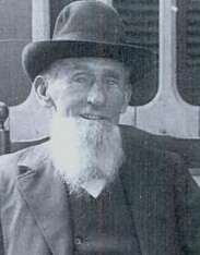 A black-and-white photograph of an elderly man with a long white beard wearing a hat