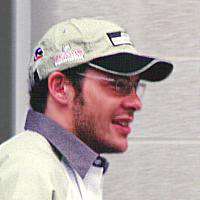 Man in his early thirties wearing a baseball cap and glasses.