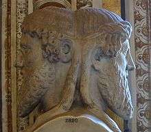 A stone bust of a man with two opposite facing heads, and curled beard.