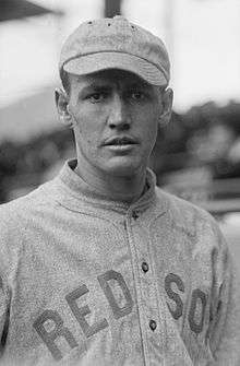 A man in a gray baseball uniform looks into the camera; he is wearing a gray baseball cap on his head and his jersey reads "Red Sox" in block type across the chest.