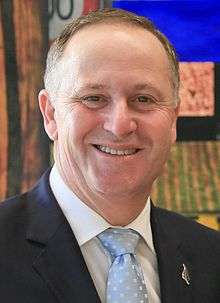 Head and shoulders of a smiling man in a dark suit and pale blue spotted tie