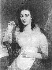 A dark-haired, exotic-looking young lady in a light-coloured dress