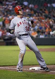 A man in a grey baseball jersey with the number 32 on the front right and a red batting helmet with the Angels logo.