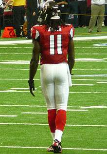 An American football player is in position on the field. He is wearing a red jersey with the number 11 across the back and white pants.