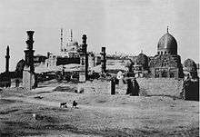 Black and white photograph of a walled city in the desert, showing domes and minarets.