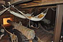 Photograph of a reconstructed ship's deck with large cannons with hammocks slung overhead
