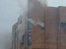 Upper portion of brick building with smoke pouring from windows