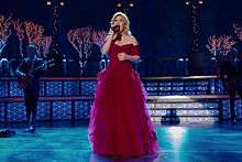 A blonde haired woman in a red dress performing in a Christmas decorated stage