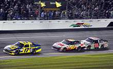 Matt Kenseth (in the blue and yellow car with the 17 number) is leading Greg Biffle in the Black, White and Red car displaying the number 16. Biffle is closely followed by Dale Earnhardt Jr. driving a car with the number 88 with a silver color scheme.