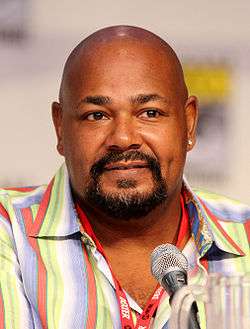 An African-American man with a bald head and a prominent goatee looking straight forward and sitting behind a microphone