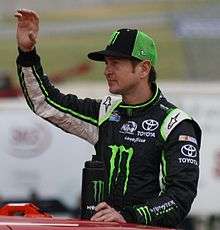 A man in his mid thirties wearing a green-and-black baseball cap and a black jacket with sponsors' logos.