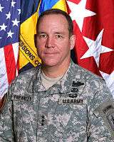 Portrait photo of Caucasian male wearing an army combat uniform with the rank of lieutenant general, Combat Infantry Badge, Basic Parachutist Badge, Air Assault Badge, and a Ranger tab standing in front of the U.S. flag, a command flag, and a lieutenant general flag.