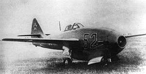 Black-and-white three-quarter view of jet aircraft on grass. The engine inlet is in the nose.
