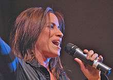 A woman holding a microphone wearing a black blouse.
