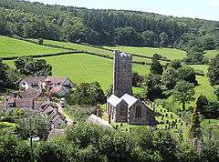 Looking down on the village with houses and stone church building with square tower.