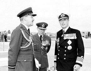 Three men in dark military uniforms with peaked caps