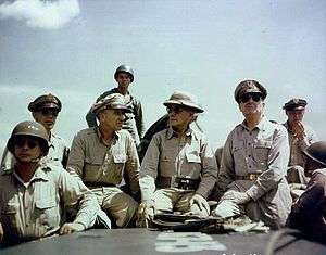 Eight men in khaki uniforms, seated.