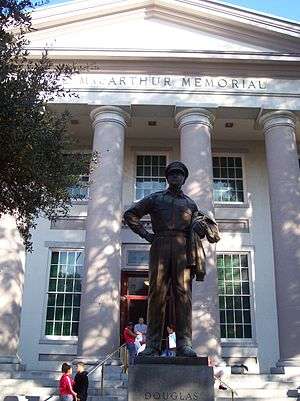 A large bronze statue of MacArthur stands on a pedestal before a large white building with columns. An inscription on the building reads: "Douglas MacArthur Memorial".