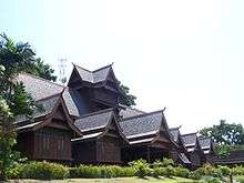 A large intricate wooden house facing right with a forest in the background