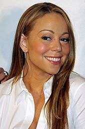 A light haired medium skin colored female smiling. The female has long hair and is wearing a white sleeved shirt that is slightly un-buttoned at the top.