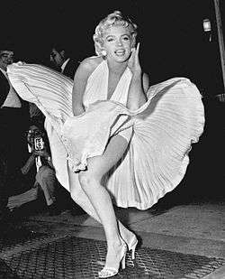 Monroe is posing for photographers, wearing a white halterneck dress, whose hem is blown up by air from a subway grate on which she is standing.
