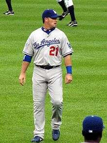 A Caucasian male wearing a baseball uniform with the number 21 and the word Los Angeles in cursive is walking forward and looking to his right.
