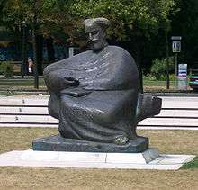 Gray statue in park of Bearded man in a robe, sitting