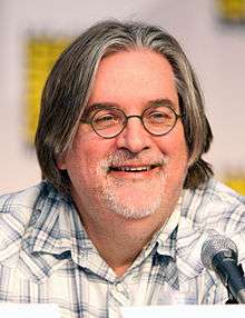 A man with shoulder length salt & pepper hair sitting in front of a microphone.