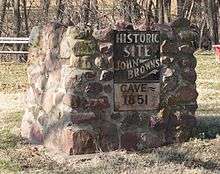 Metal sign on stone pier, reading "Historic Site - John Brown's Cave - 1851"