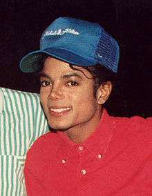 A picture of a man wearing a red shirt and blue cap while smiling