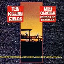 A rectangular slit on a grey background featuring a sunset photo of a work site. Yellow text is at the bottom of the image; "This is a story of war and friendship, anguish and honour. A ruined country and one man's will to live...". Two red squares at the top left and right say the album title The Killing Fields and Mike Oldfield Original Film Soundtrack.