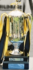 The Milk Cup trophy is standing upright with black and yellow ribbons tied to the handles, to represent Oxford United's colours
