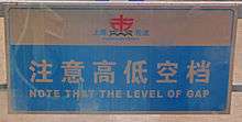 A light-colored sign with Chinese characters and "Note that the level of gap" written on it in blue